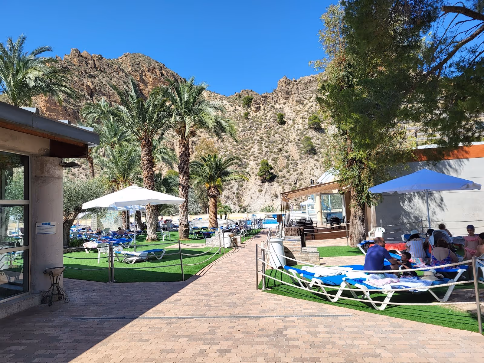 Outdoor pool area with blue lounge chairs and white umbrellas at Balneario de Archena surrounded by rocky hills in Murcia Spain.