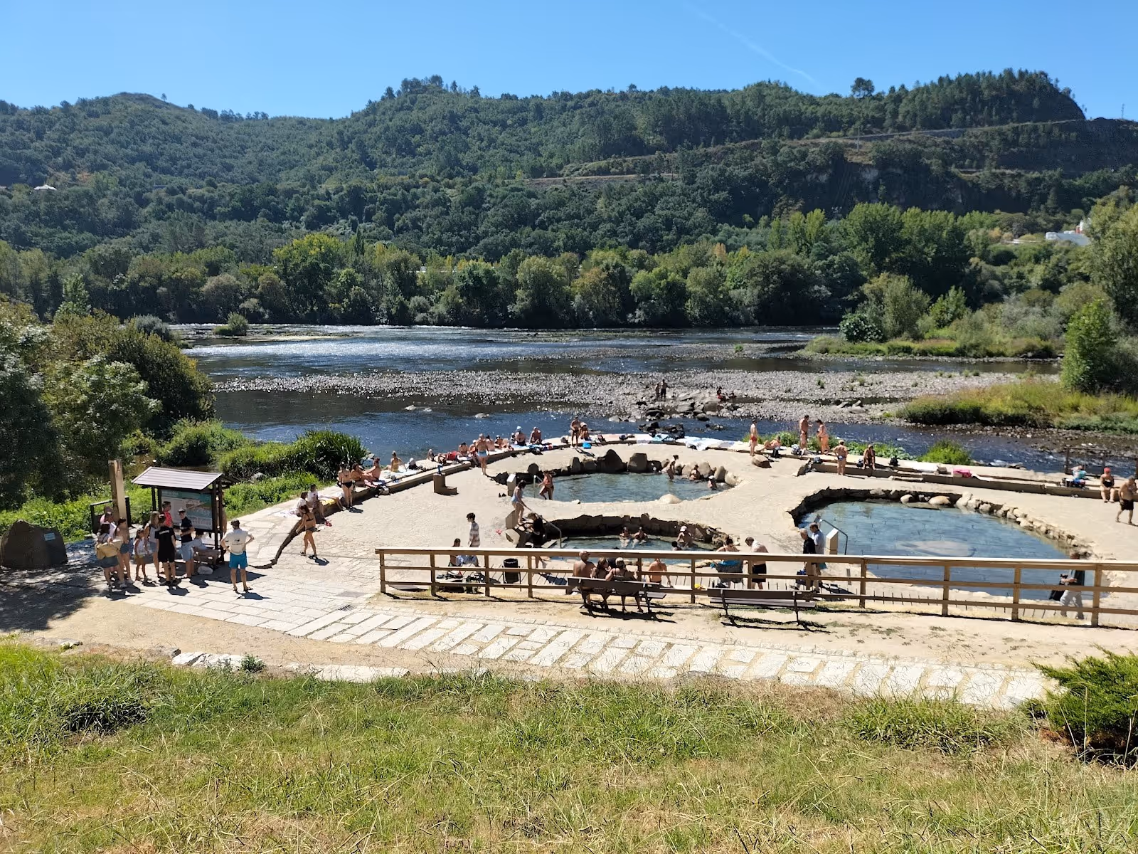 Outdoor hot spring pools at Termas de Outariz in Ourense Spain beside a flowing river with surrounding green hills.