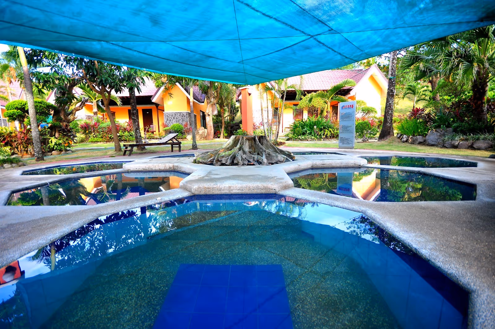 Outdoor hot spring pool at 88 Hot Spring Resort with shade cloth cover surrounded by tropical plants and cottages in Calamba City Philippin.