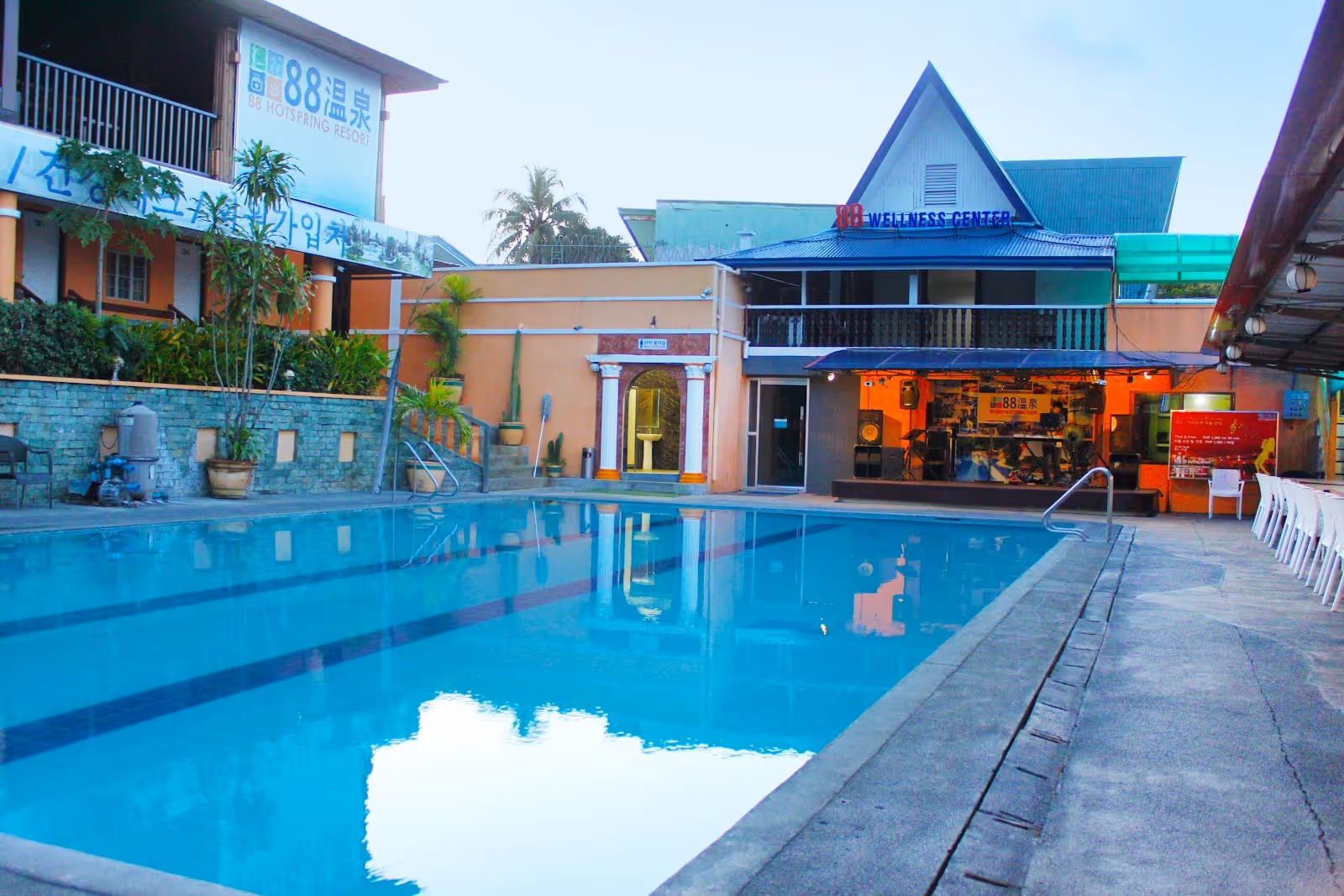 Calm outdoor pool at 88 Hot Spring Resort reflecting buildings with signage and vegetation, creating a serene atmosphere in Calamba City.