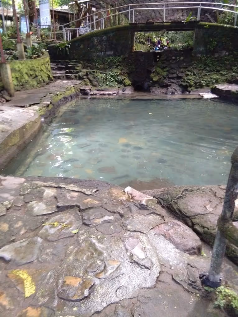 Natural stone-bordered mineral pool with clear water surrounded by greenery at Ardent Hot Spring in Mambajao.