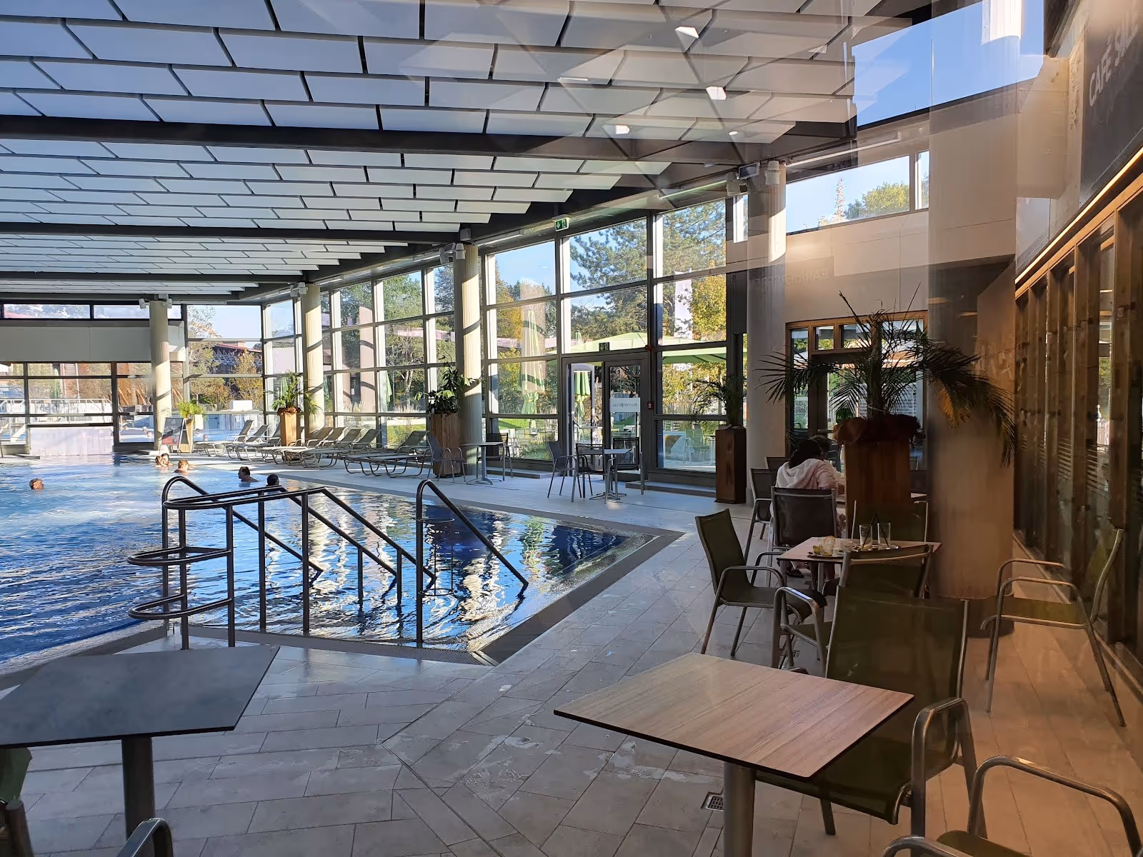 Indoor spa pool with people soaking and tables with chairs near large windows providing natural light at Borde Therme Bad Sassendorf.