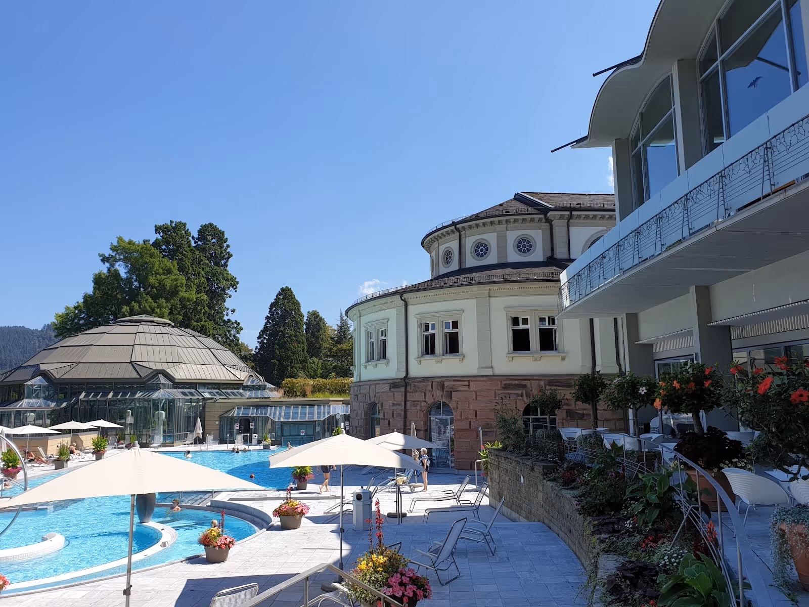 Large dome-shaped building next to an outdoor pool area with umbrellas and lounge chairs at Cassiopeia Therme Badenweiler near Badenweiler.