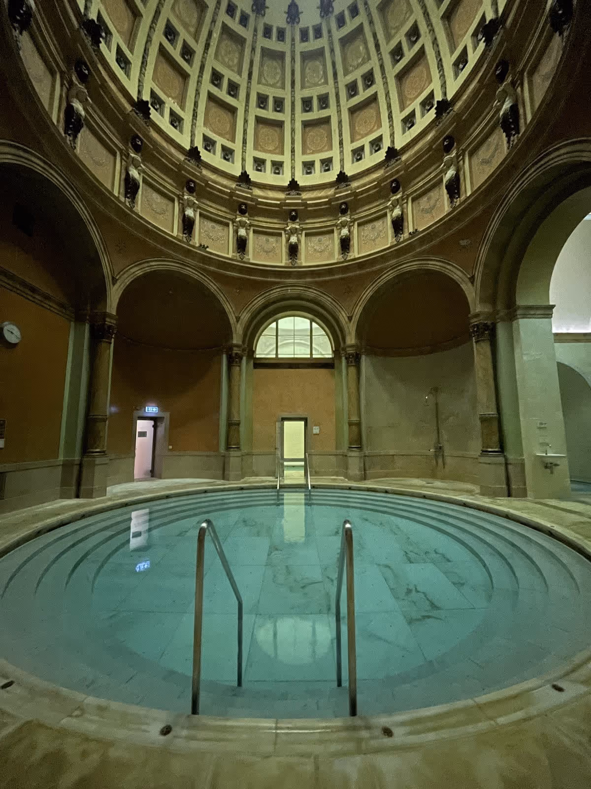 Circular indoor mineral pool with steps and columns under a domed ceiling with intricate artwork at Friedrichsbad hot spring in Germany.