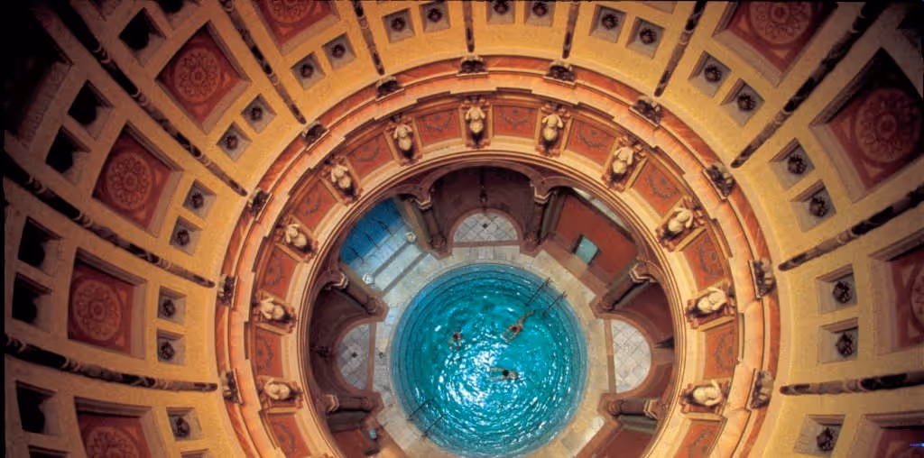 Looking down into a round indoor hot spring pool at Friedrichsbad with terracotta decorative arches and statues in Baden-Baden Germany.