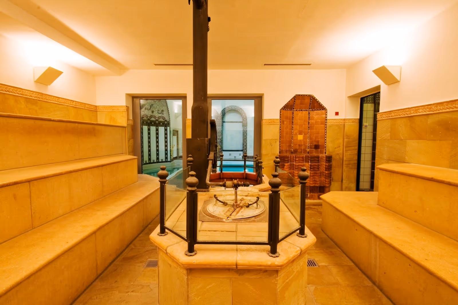 Warm-lit indoor foyer with stone benches along the walls and a metal column in the center at Kaiser-Friedrich-Therme near Wiesbaden.