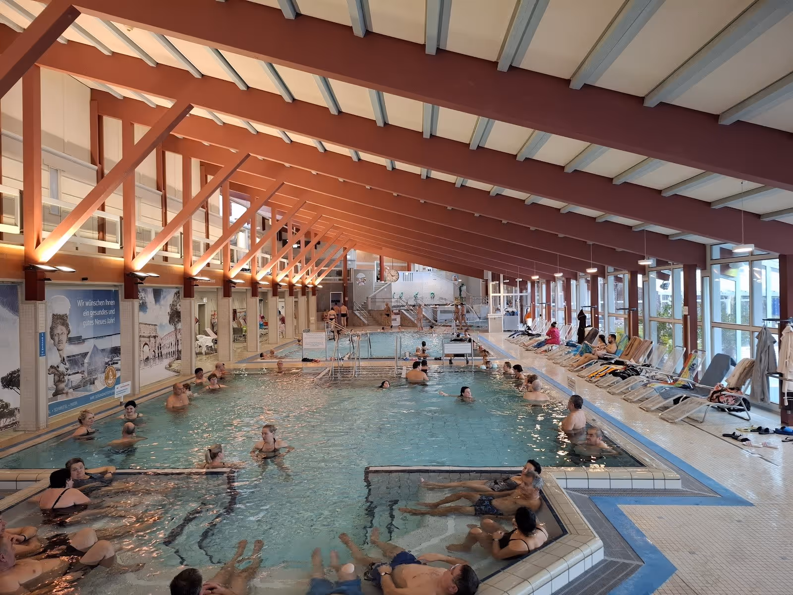 Indoor thermal pool at Limes-Therme Bad Goegging with steam rising and several people relaxing under wooden beam ceiling in Germany.