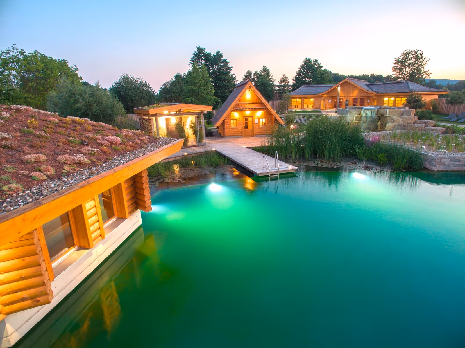 Natural outdoor pool with turquoise water surrounded by wooden cottages and green plants at Obermain Therme in Bad Staffelstein Germany.