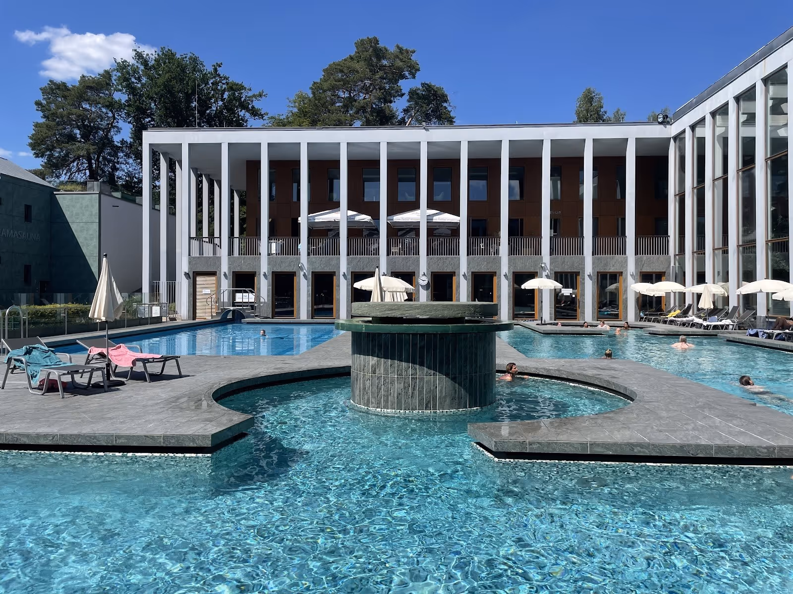 Outdoor pool area at SaarowTherme in Bad Saarow Germany with lounge chairs, umbrellas, and a modern building on a clear sunny day.
