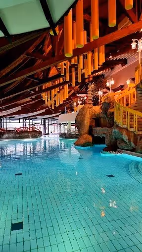 Indoor mineral pool at Taunus Therme with glowing warm water, wooden beams, large windows, and bright orange hanging lights.