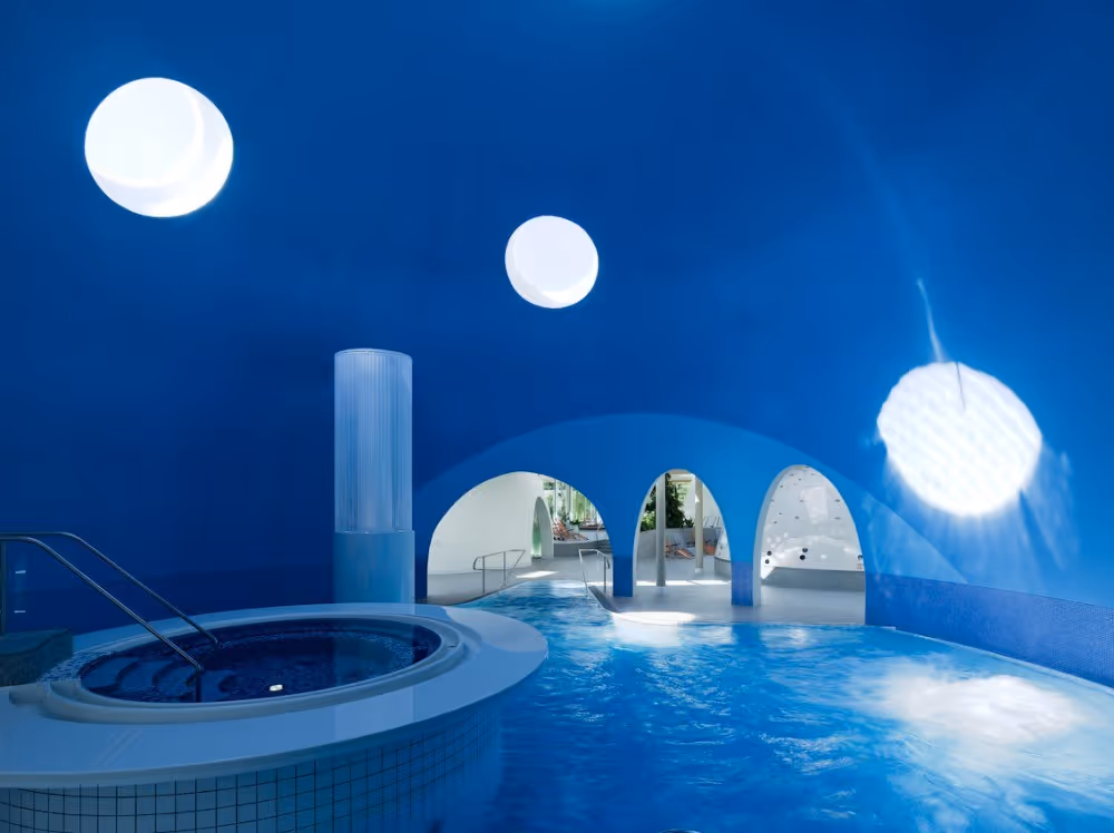 Indoor hot spring pool under a large blue dome with round skylights and archways at Therme Bad Aibling in Bad Aibling, Germany.