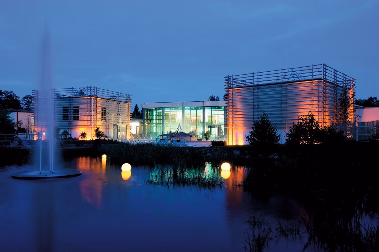Therme Bad Steben outdoor pool at dusk with illuminated modern buildings reflecting in a calm water pond in Bad Steben germany.