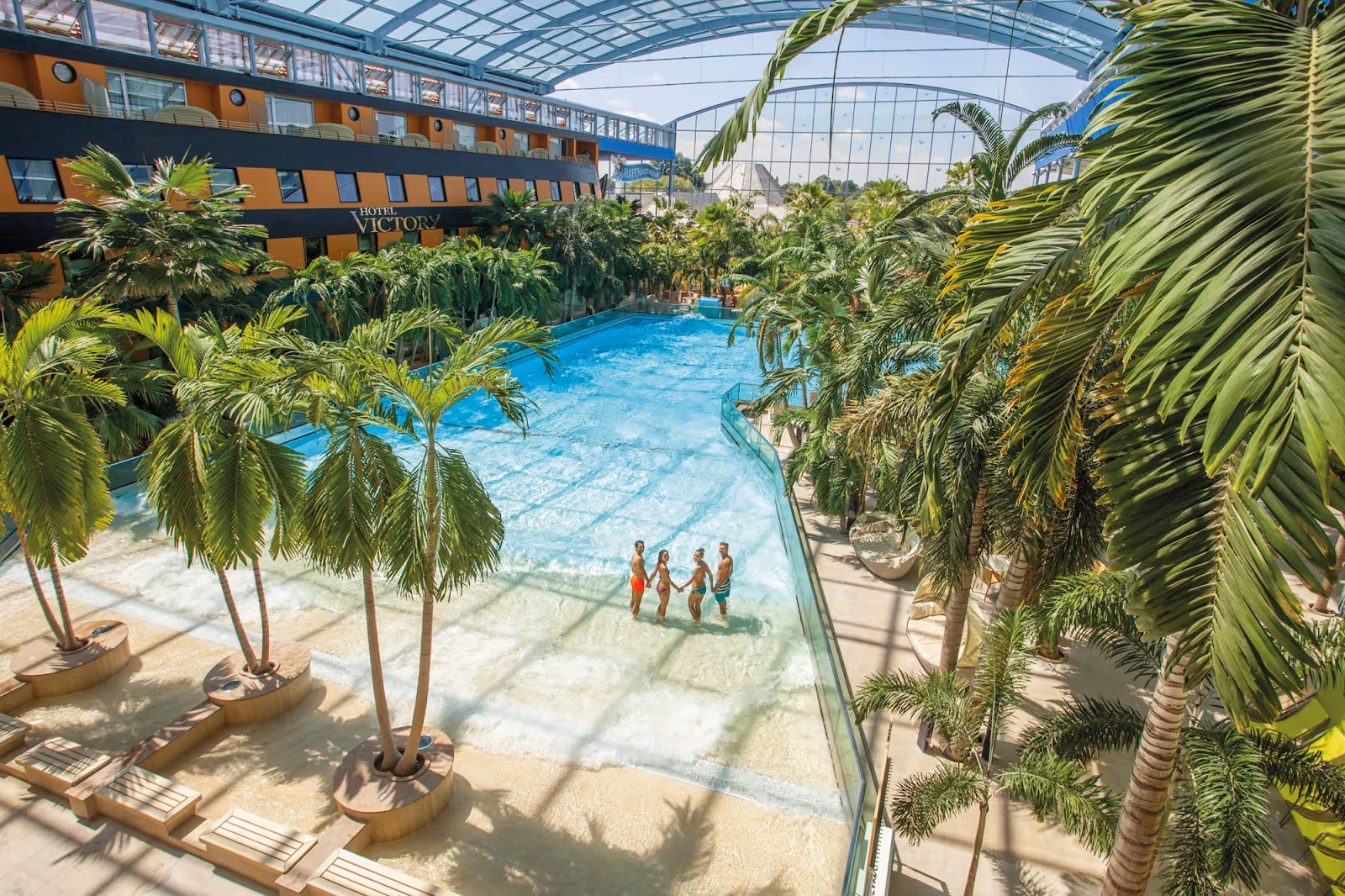 Indoor hot spring pool at Therme Erding, Germany, surrounded by lush palm trees and a hotel building under a large glass roof.