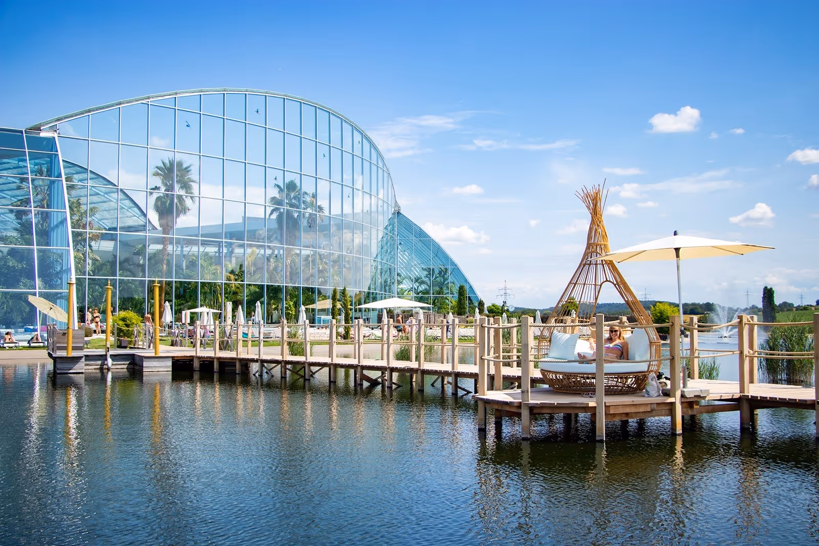 Outdoor spa pool at Thermen & Badewelt Sinsheim featuring a wooden boardwalk, sunshade umbrellas, and a reflective water pond in Sinsheim G.
