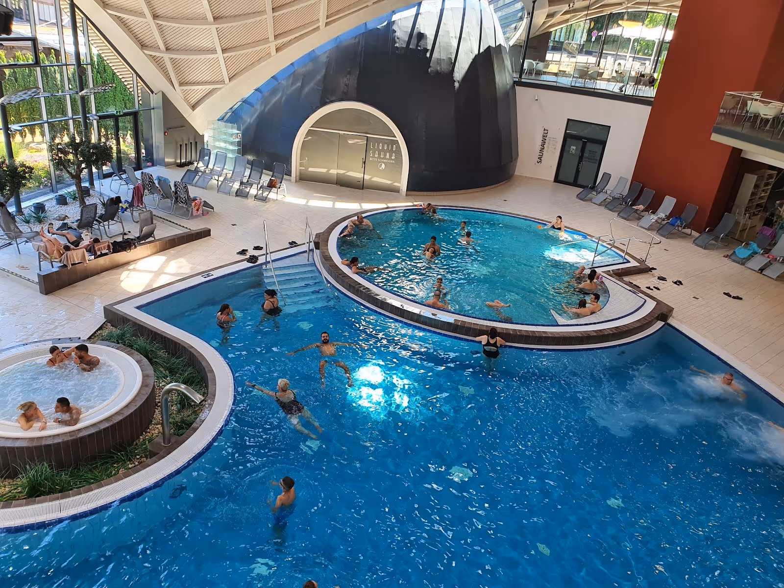 Indoor swimming pools at Toskana Therme Bad Orb filled with people relaxing and large skylight ceiling overhead.
