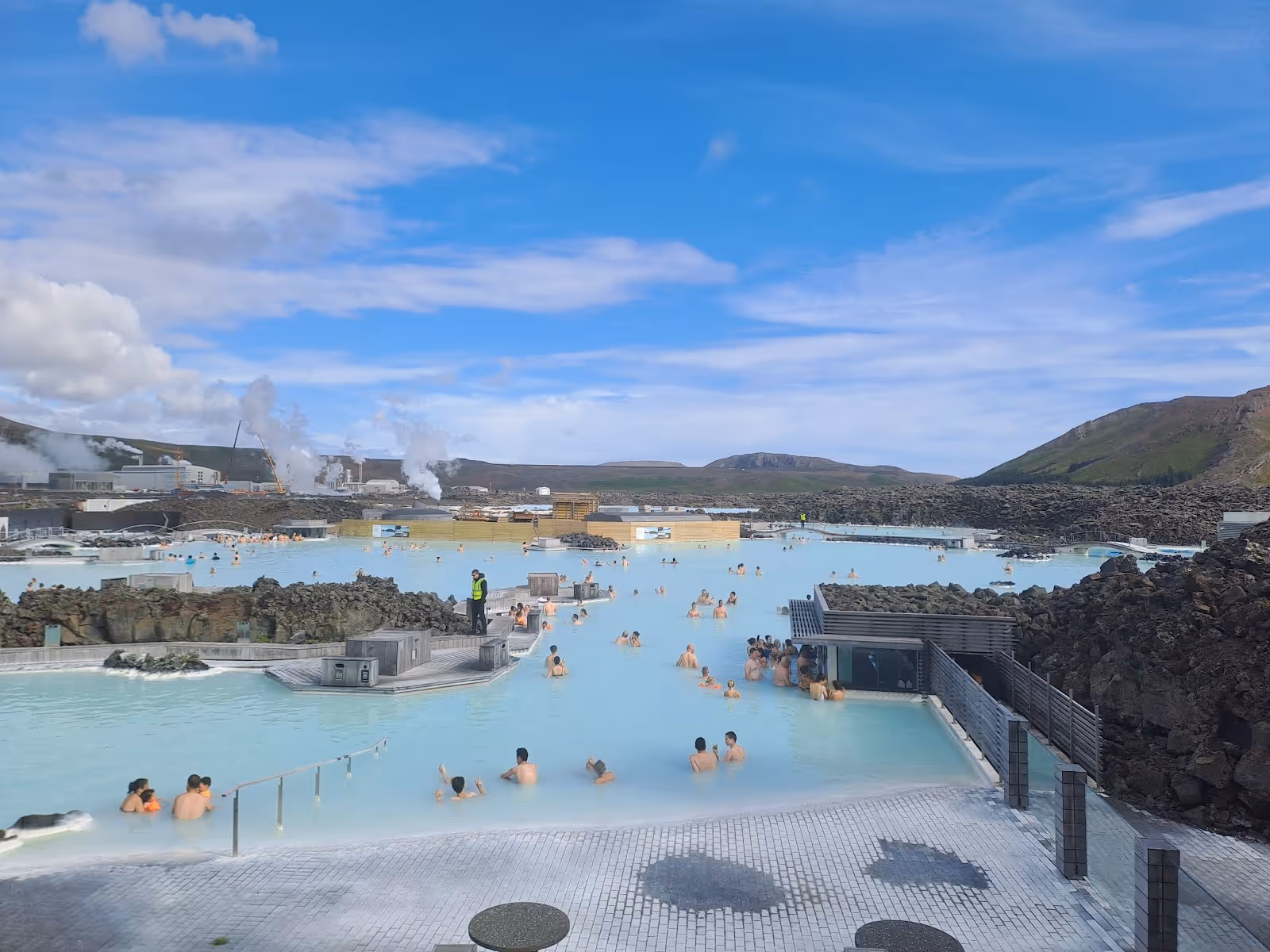 Blue Lagoon hot spring pool with milky blue water and people relaxing near black lava rocks under a clear blue sky in Iceland.