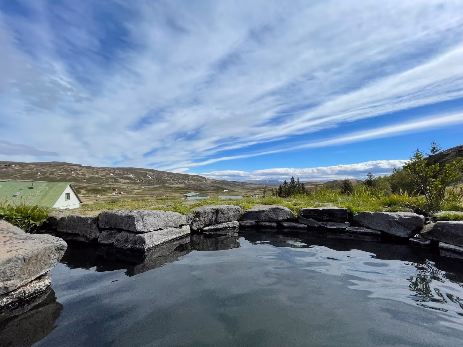 Natural hot spring pool at Gudrunarlaug with stone edges set against a backdrop of rolling hills near Budardalur Iceland.