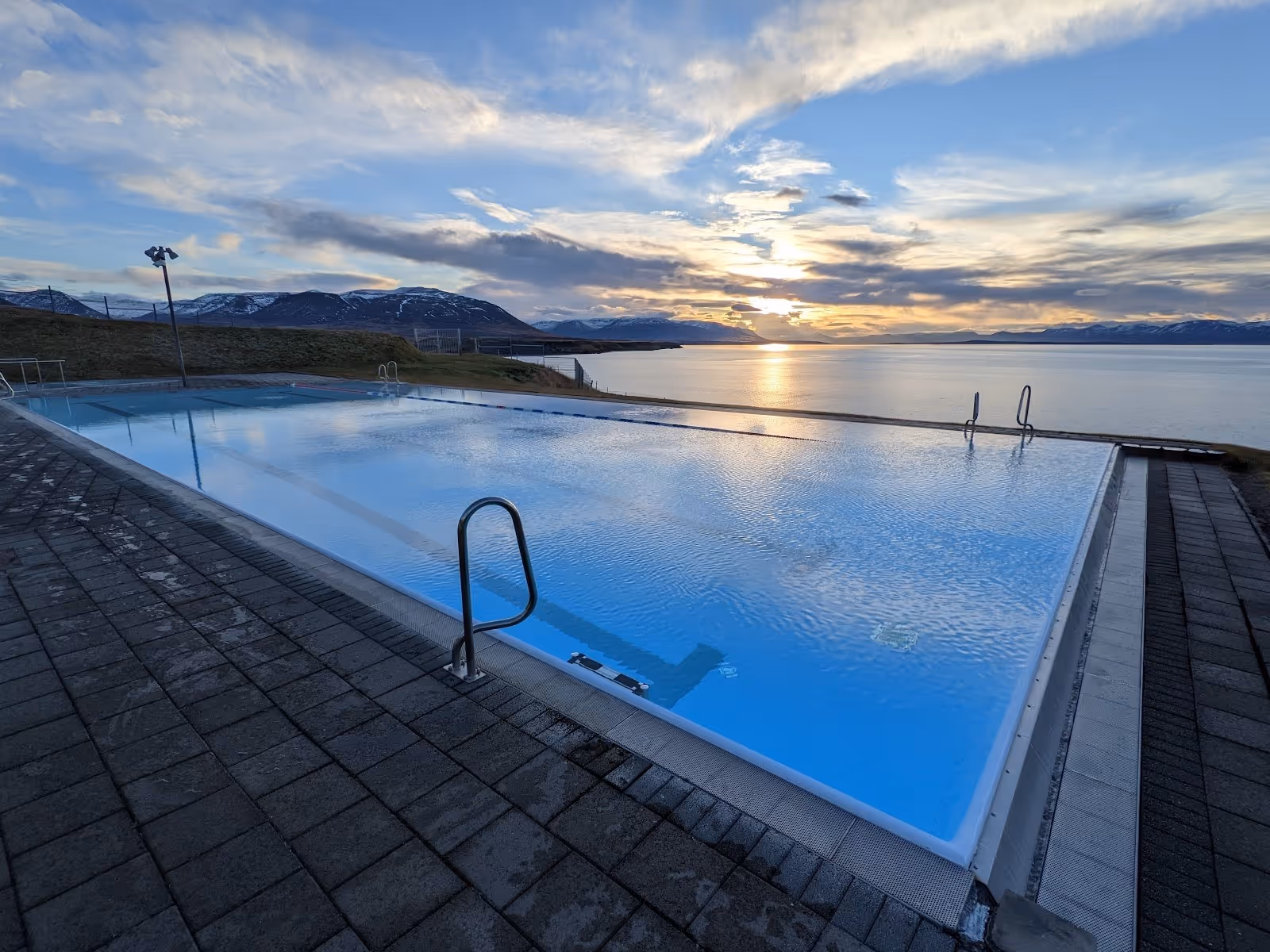 Hofsos Swimming Pool outdoor pool at sunset with calm water reflecting sky and distant snowy mountains near Hofsos Iceland.