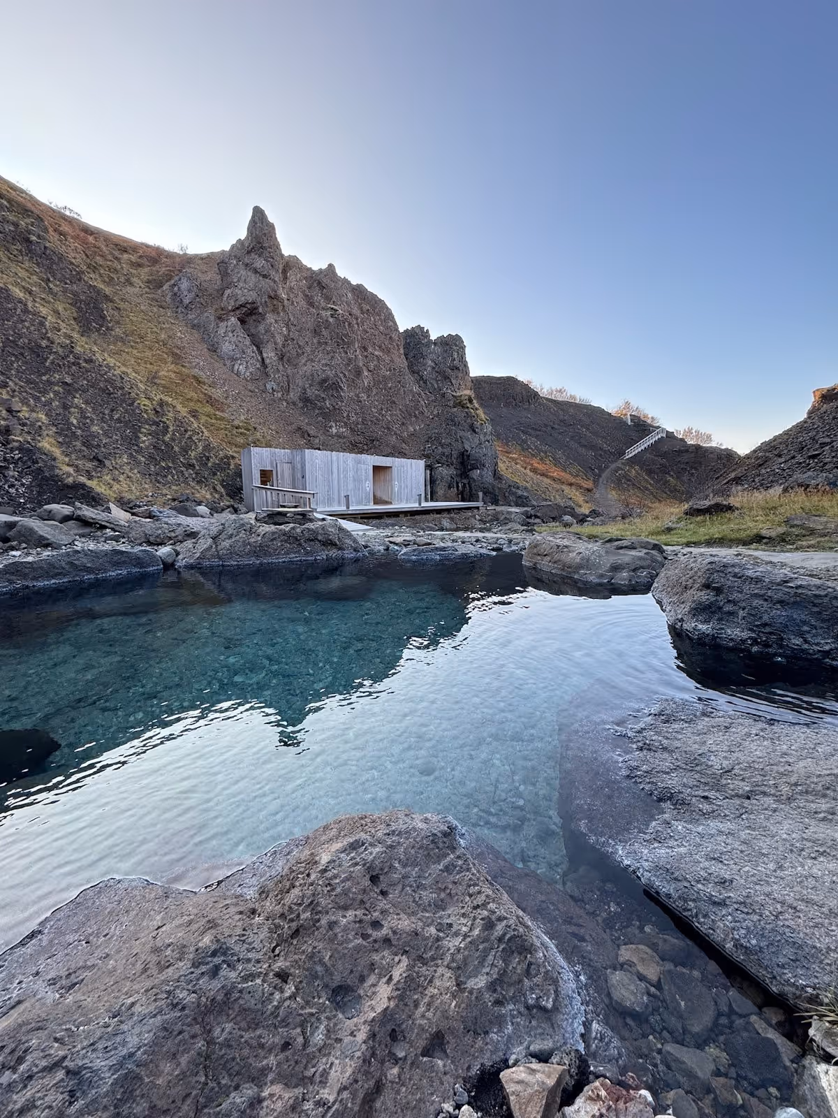 Natural hot spring pool with smooth rocky edges and a wooden platform set against steep cliffs at Husafell Canyon Baths Iceland.