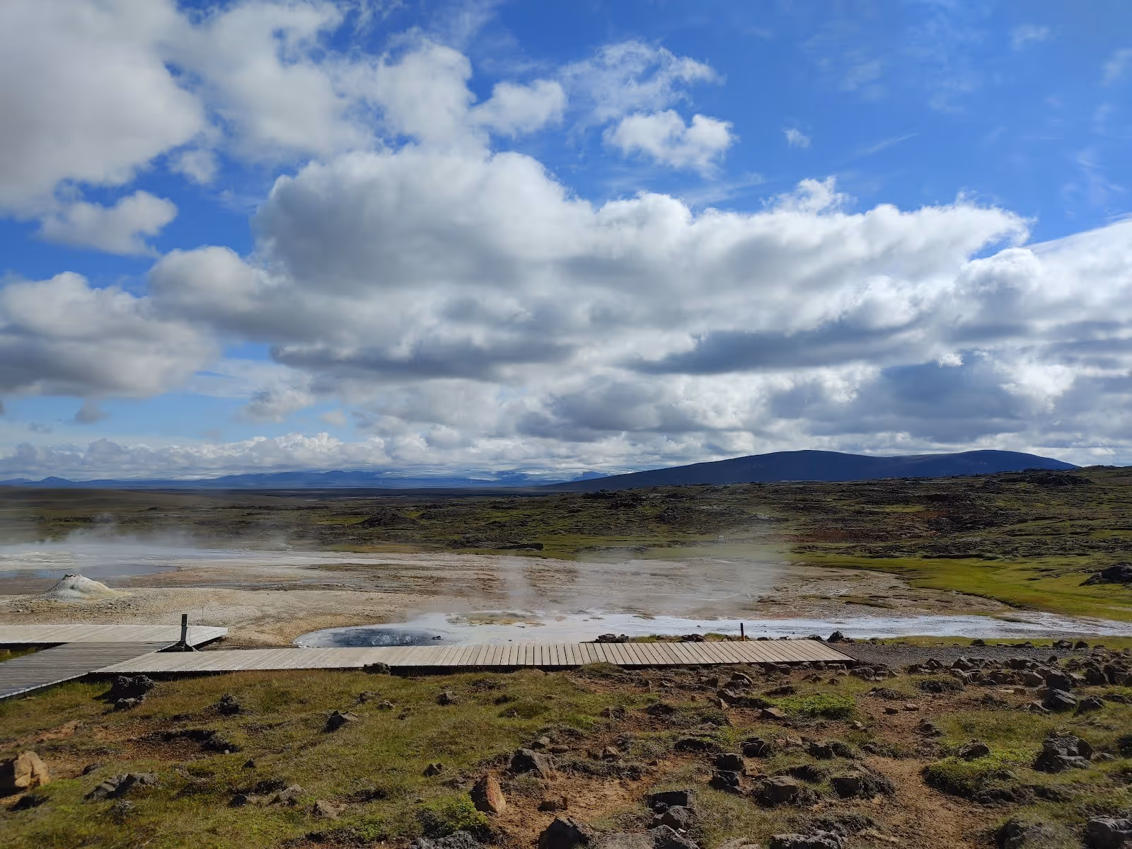Wooden walkway over a snowy geothermal landscape with steam rising from hot springs and rocky mossy ground near Hveravellir in Iceland.