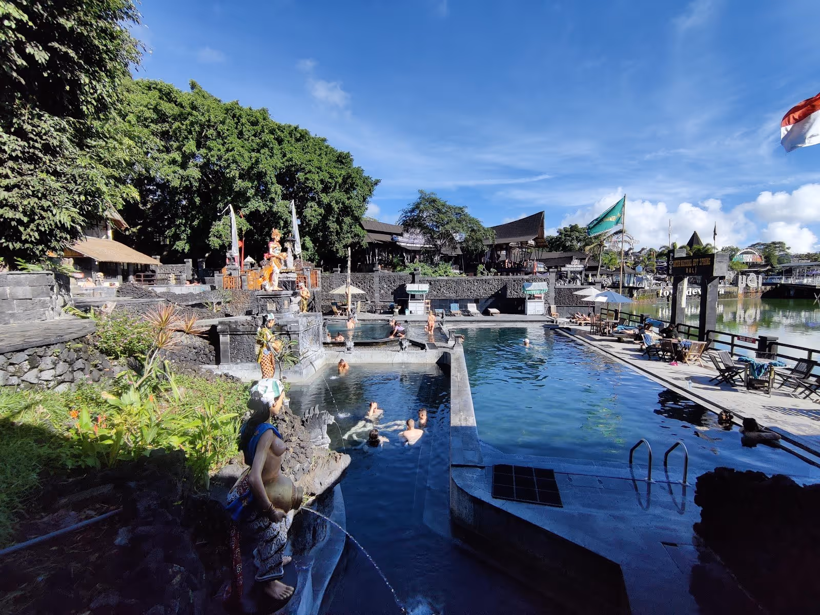 Outdoor hot spring pools with several people soaking, surrounded by stone terraces and tropical greenery in Bali.