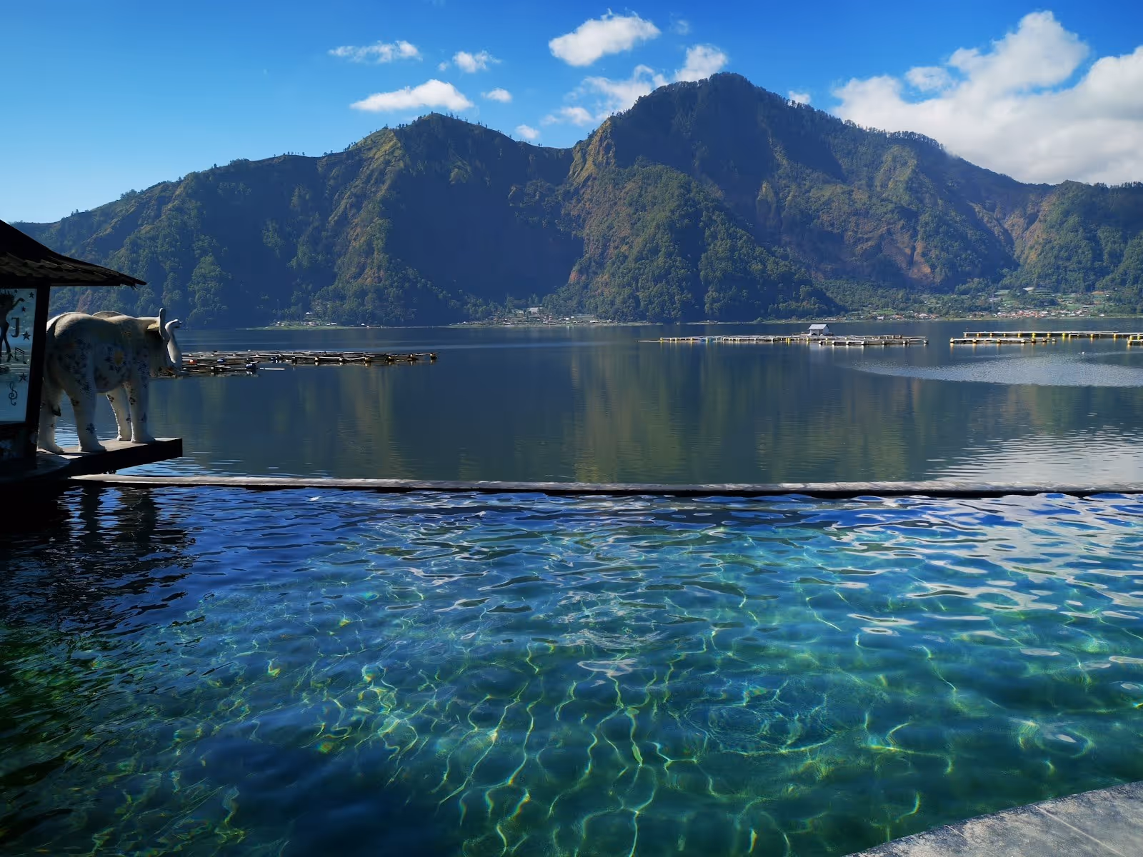 Clear infinity style hot spring pool reflecting sunlight with a mountain lake view near Kintamani Bali Indonesia.