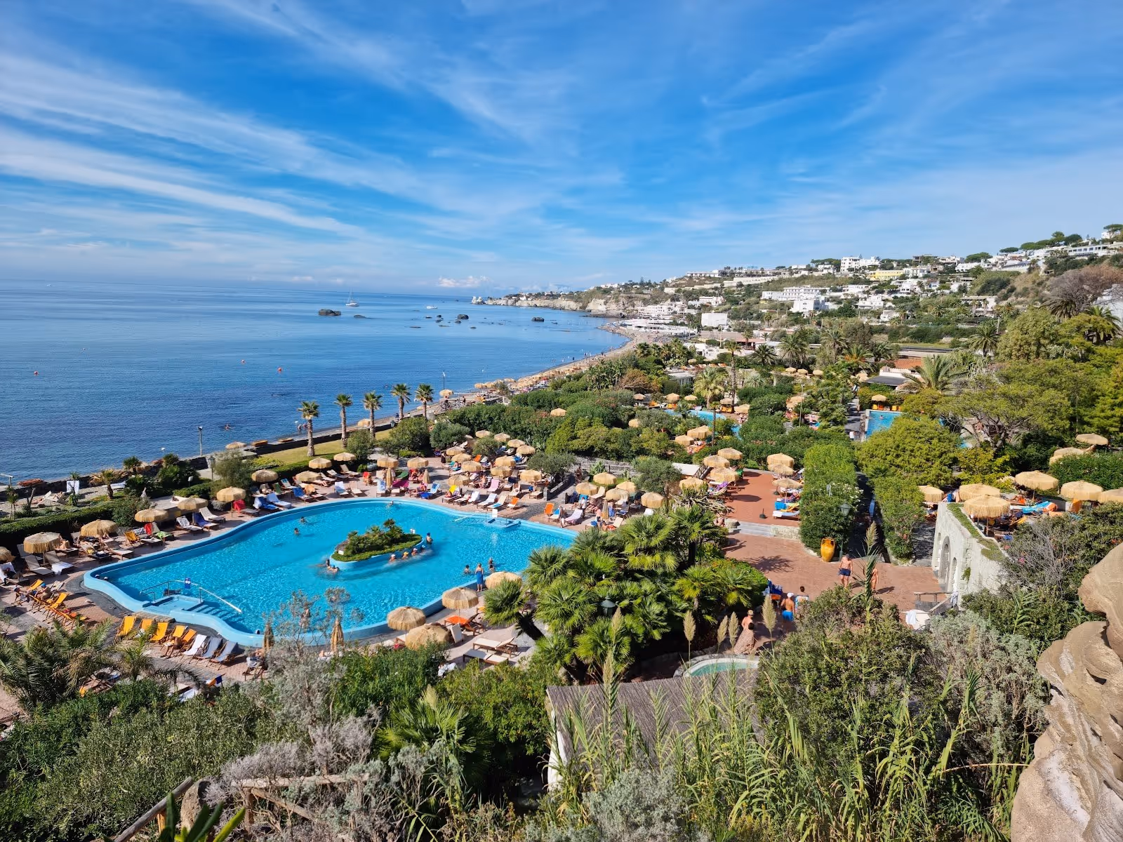 Outdoor hot spring pool at Giardini Poseidon Terme in Forio Ischia Italy with bright blue water and umbrellas near the sea shore.