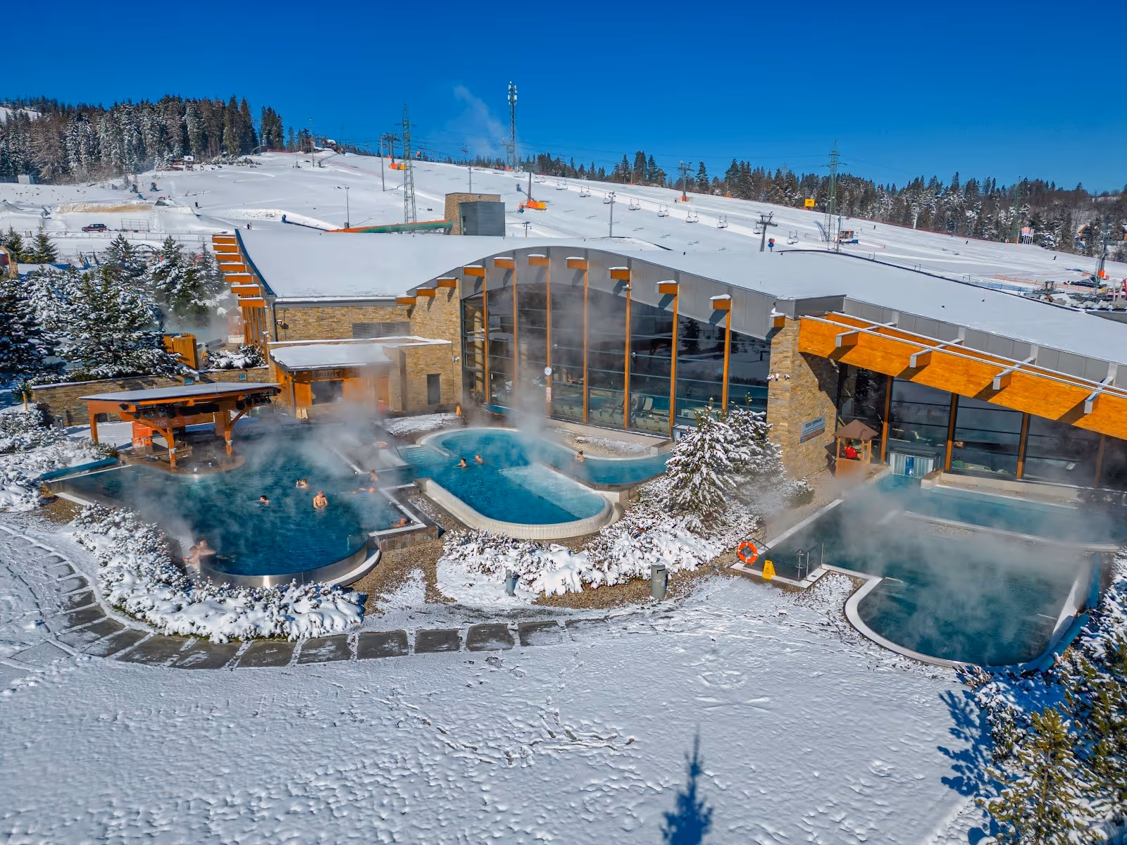 Aerial view of Terma Bania's outdoor steaming pools surrounded by snow with ski slopes in Bialka Tatrzanska Poland.