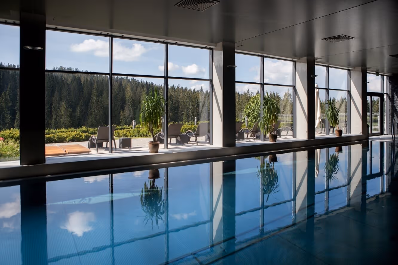 Indoor pool at Termy BUKOVINA with large windows showing an outdoor view of pine trees and lounge chairs in Bukowina Tatrzanska Poland.