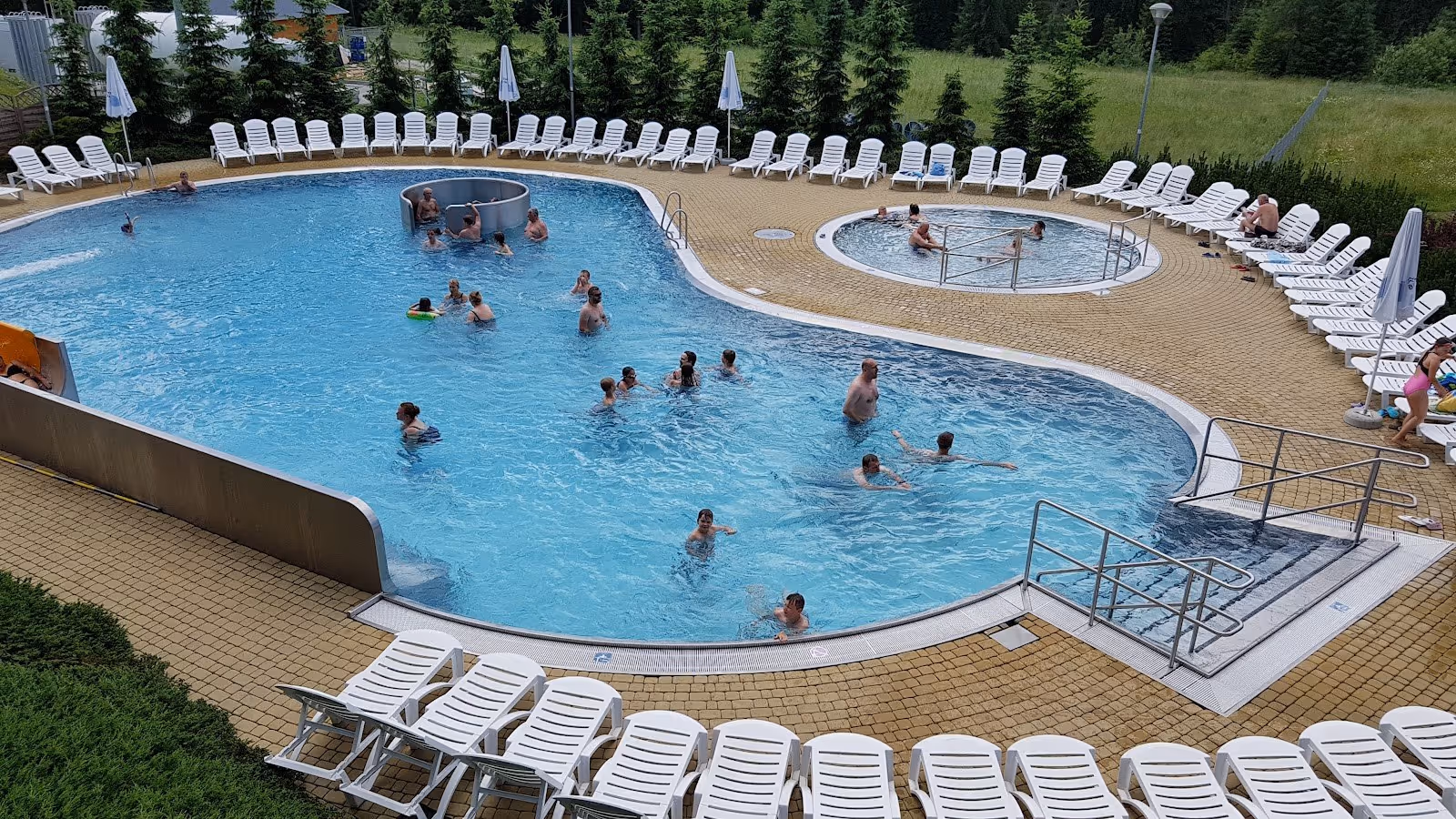 Outdoor hot spring pool at Termy BUKOVINA with several people swimming and white lounge chairs around the deck in Bukowina Tatrzanska Polan.