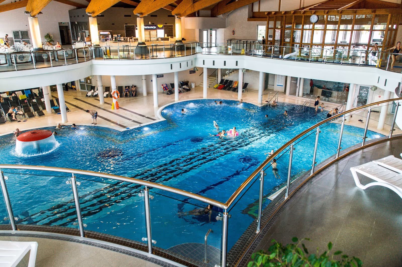 Indoor swimming pool with a large open area, surrounded by a balcony and wooden ceiling beams at Termy BUKOVINA in Bukowina Tatrzanska Pola.
