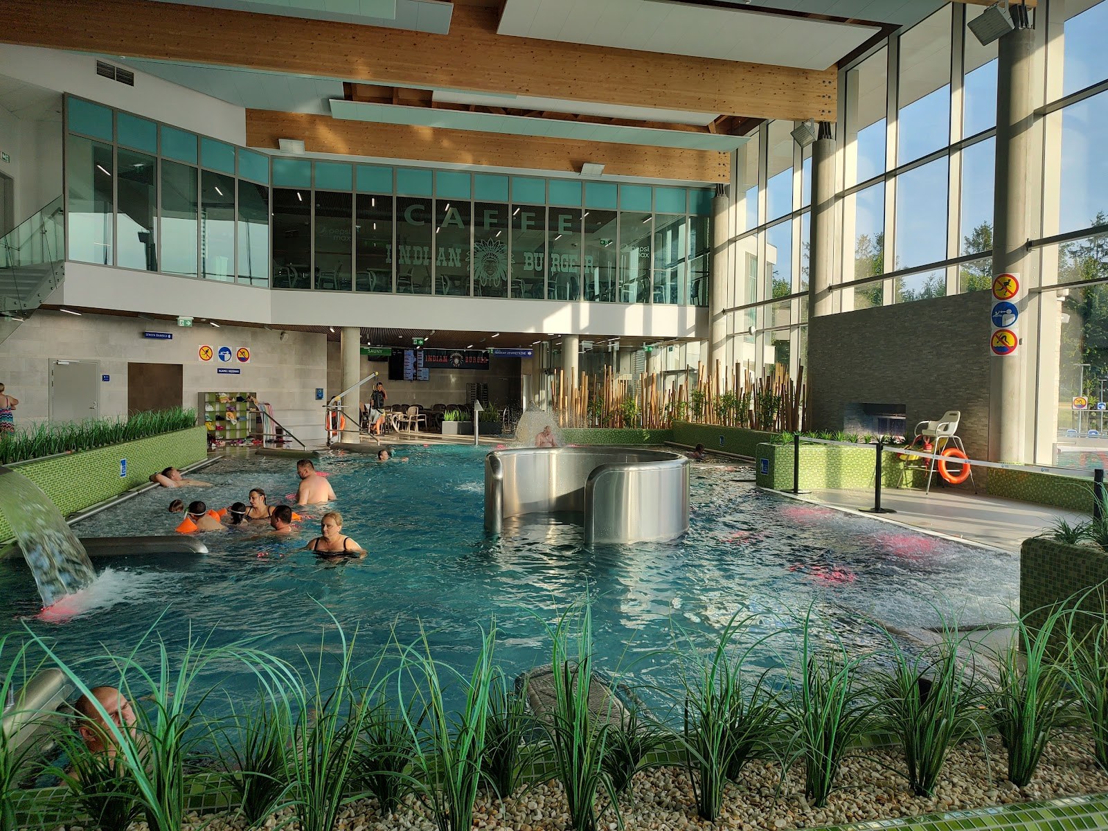 Indoor hot spring pool at Termy Poddebice with large windows, wooden beams, and guests soaking near water jets.