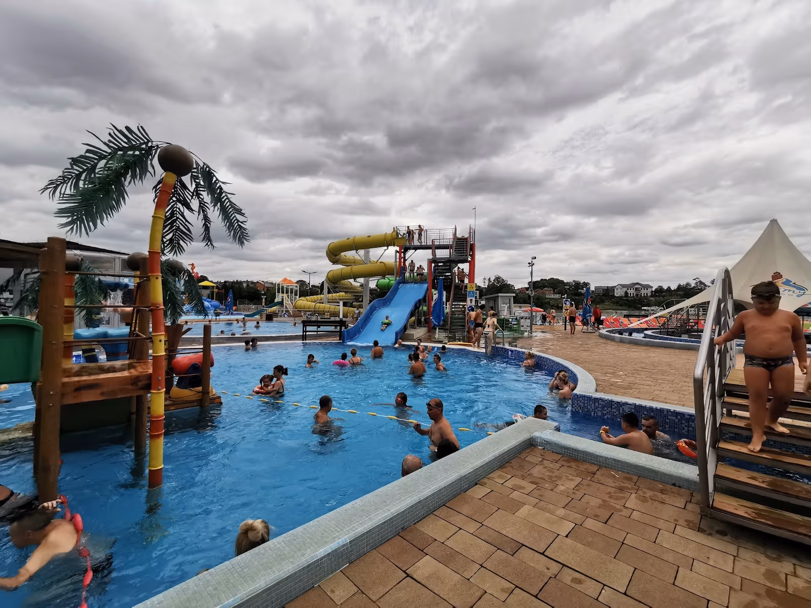 Outdoor pool area at Termy Uniejow in Uniejow Poland featuring water slides, play structures, and swimmers in a spacious pool.