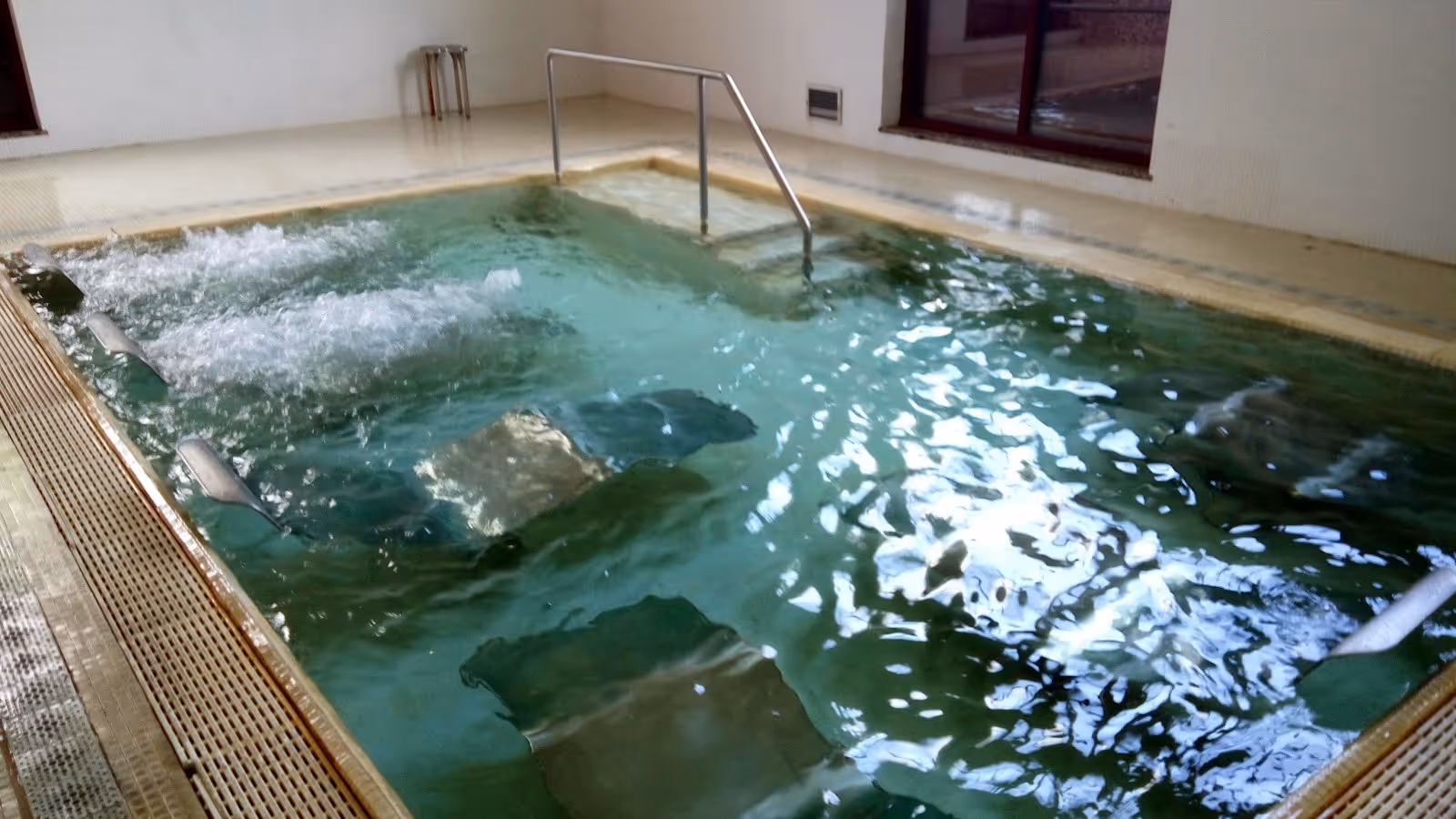 Spacious indoor mineral pool with bubbling water jets and stainless steel handrails at Termas de Moncao, located in Moncao Portugal.
