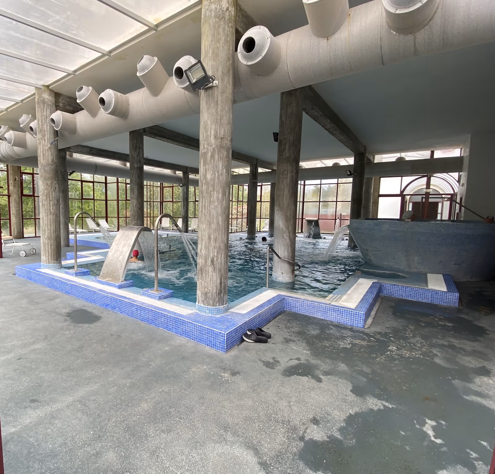 Indoor hot spring pool with blue mosaic tiles and multiple water jets under exposed concrete beams in Termas de Moncao near Moncao Portugal.