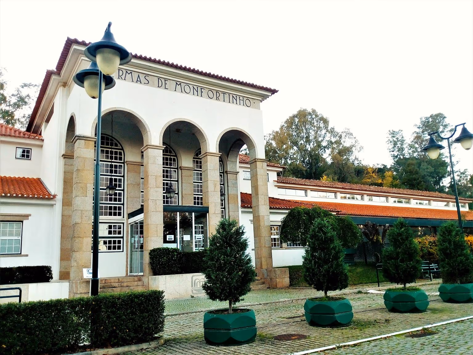 Front exterior of Termas de Monfortinho building with tall stone pillars and arched windows under a cloudy sky in Monfortinho Portugal.