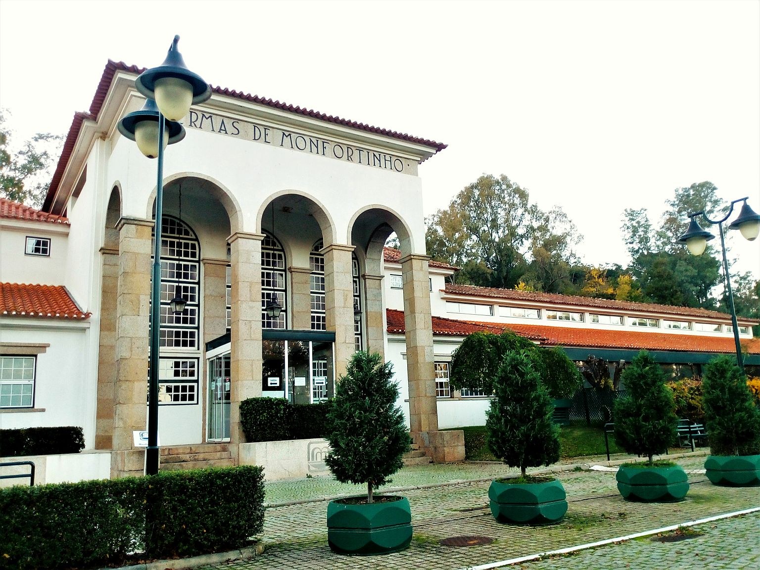 Front exterior of Termas de Monfortinho building with tall stone pillars and arched windows under a cloudy sky in Monfortinho Portugal.