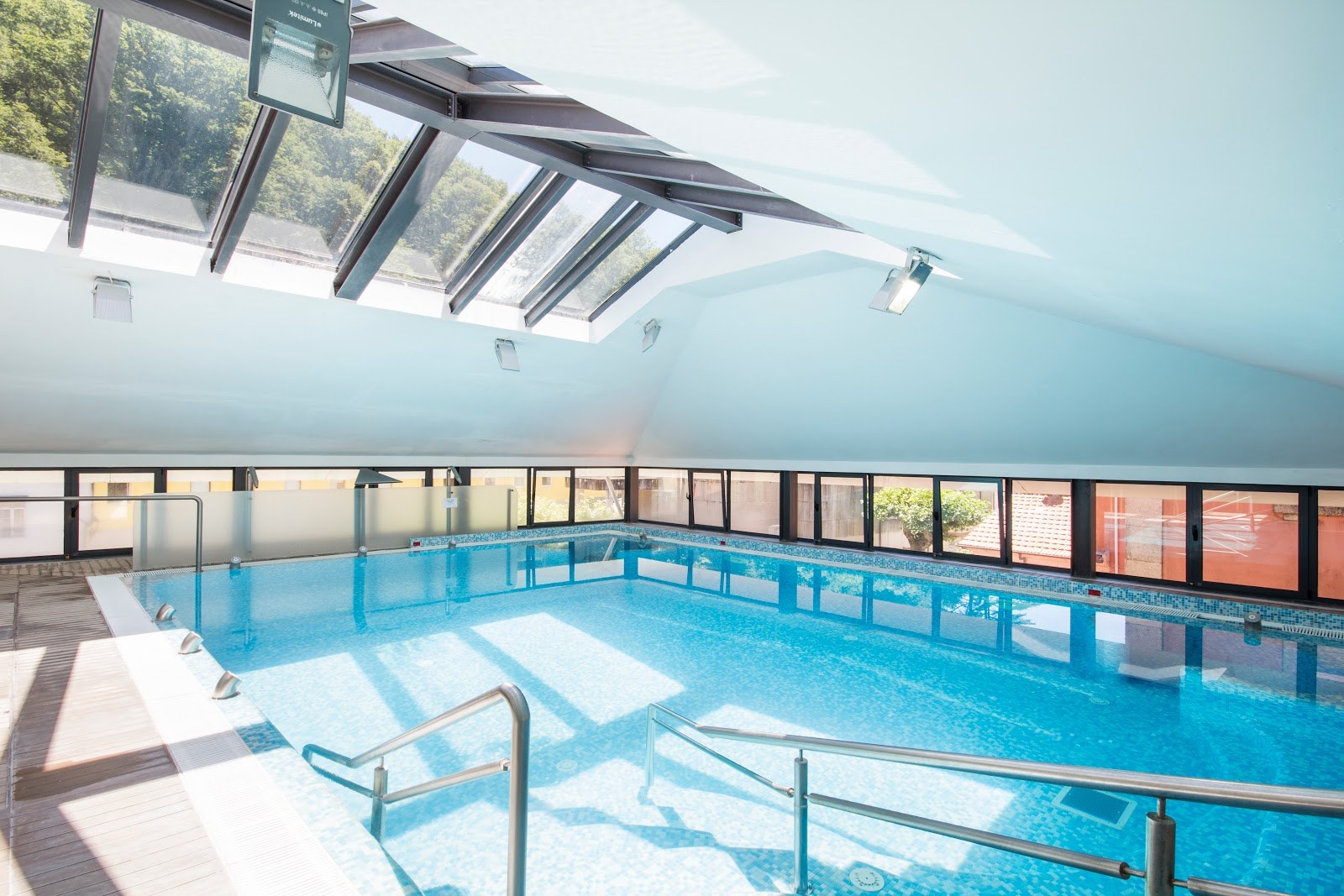 Indoor hot spring pool with handrails and large windows letting in natural light at Termas do Geres near Geres Portugal.
