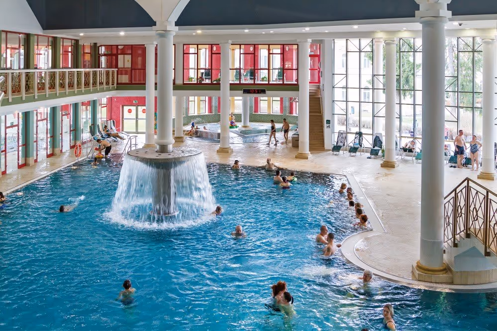 Indoor pool at Aquaforum Frantiskovy Lazne featuring a central water fountain and large windows letting in natural light in Czechia.