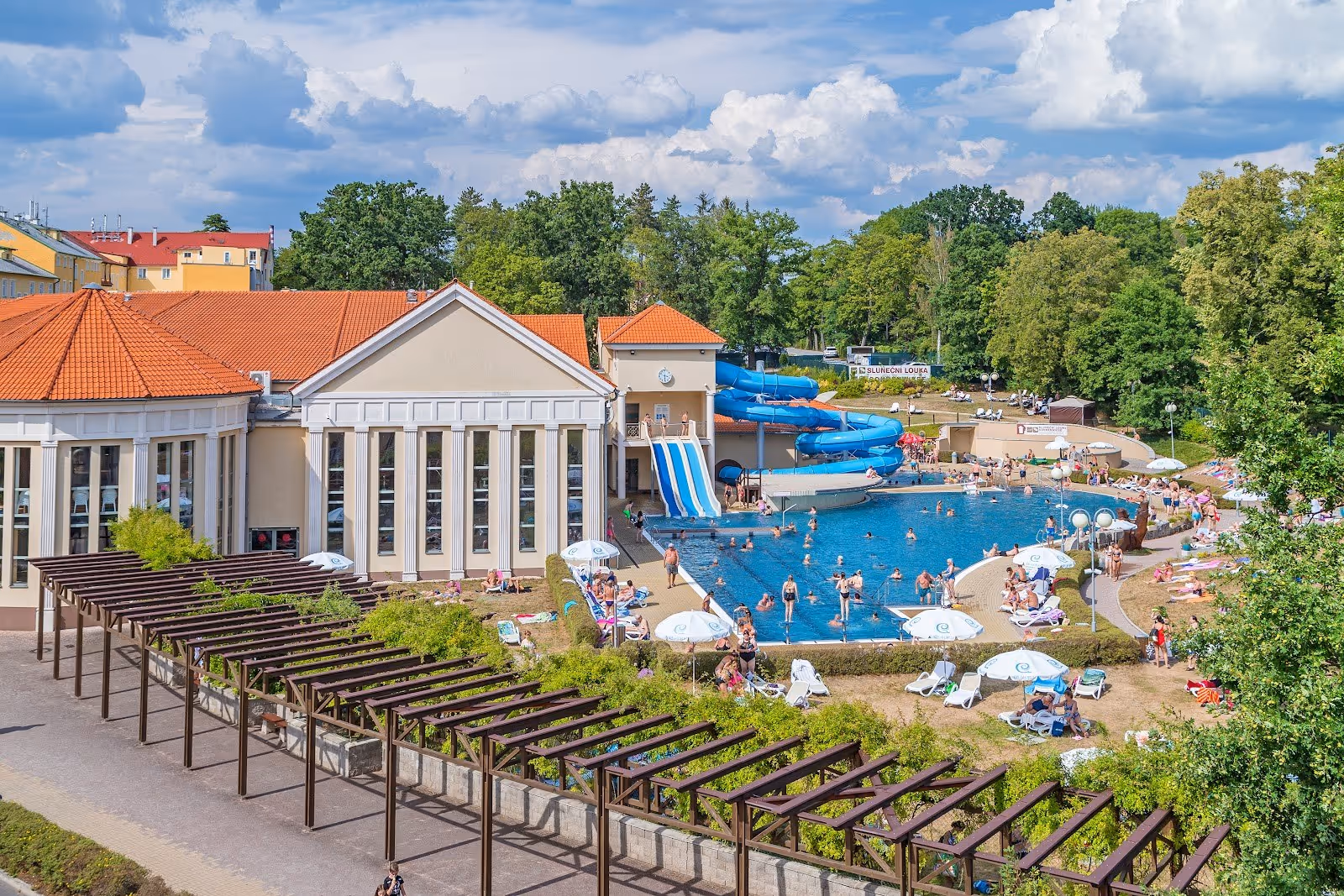 Outdoor pool at Aquaforum Frantiskovy Lazne with blue water slides and people swimming on a sunny day in Frantiskovy Lazne, Czechia.