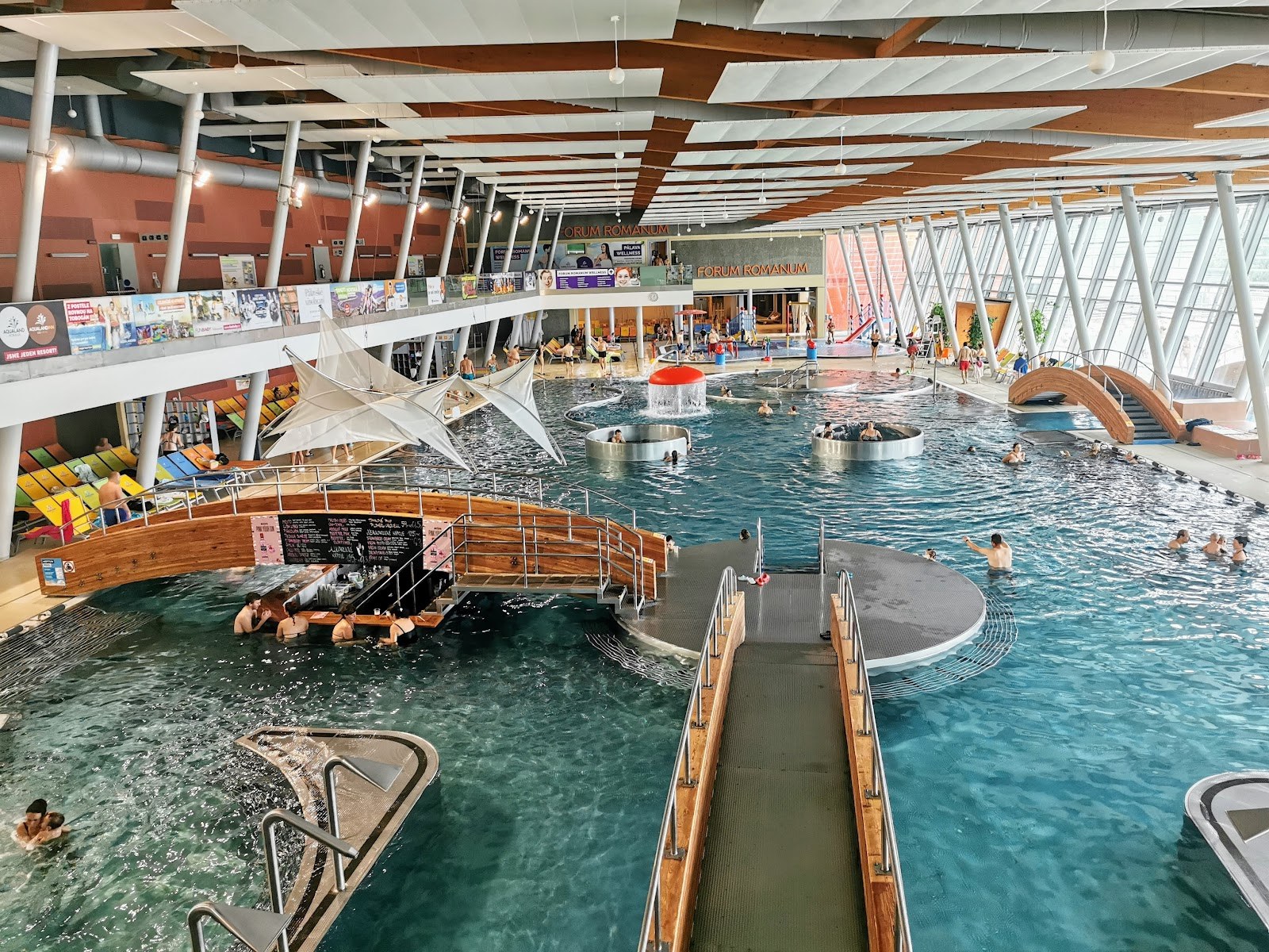 Indoor hot spring pool at Aqualand Moravia in Pasohlavky Czechia with wooden bridges and circular seating areas in clear water.