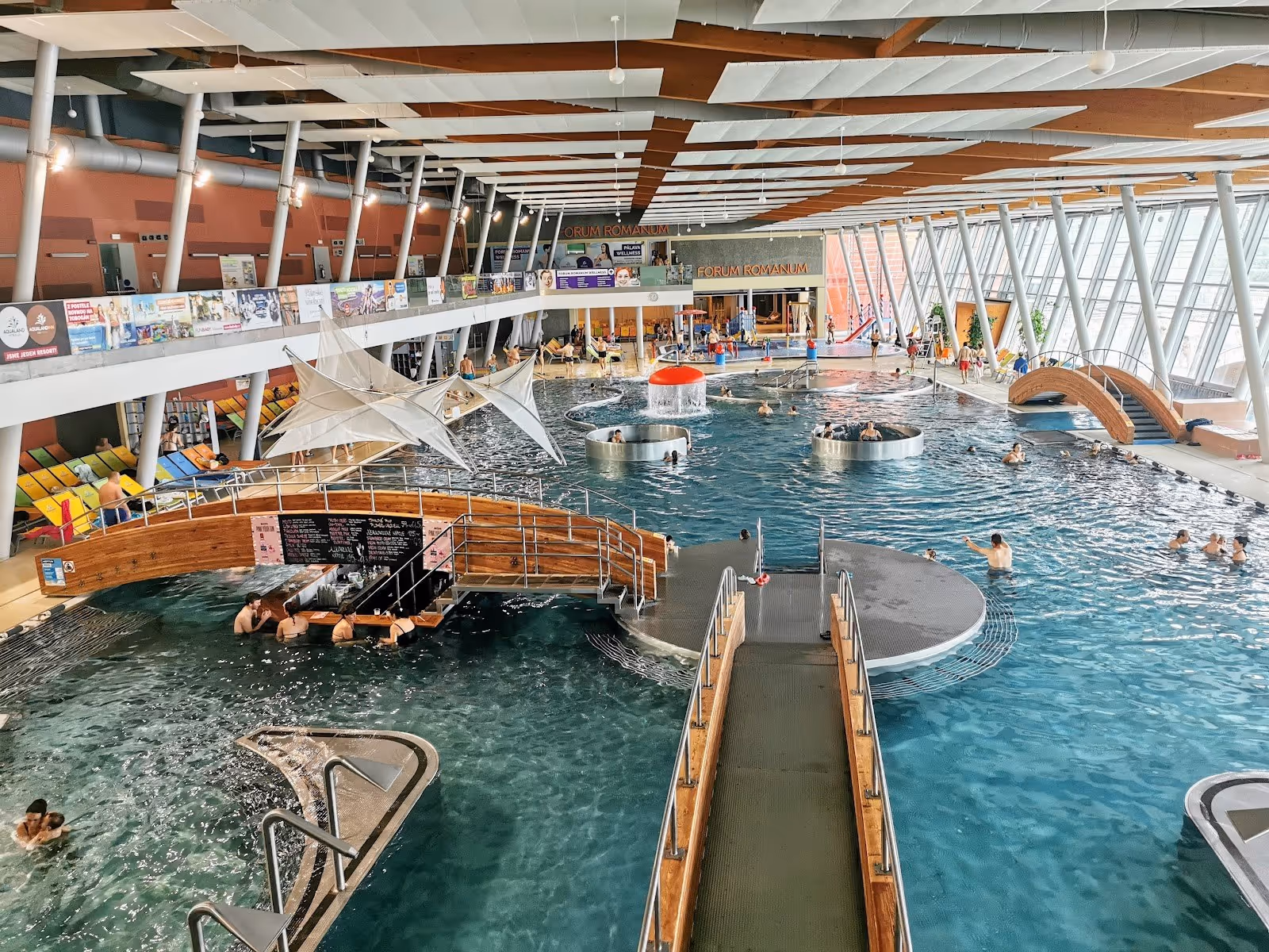 Indoor hot spring pool at Aqualand Moravia in Pasohlavky Czechia with wooden bridges and circular seating areas in clear water.