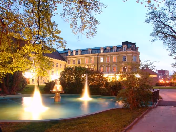 outdoor hot spring pool with illuminated water fountains in front of historical building during dusk in teplice czechia.