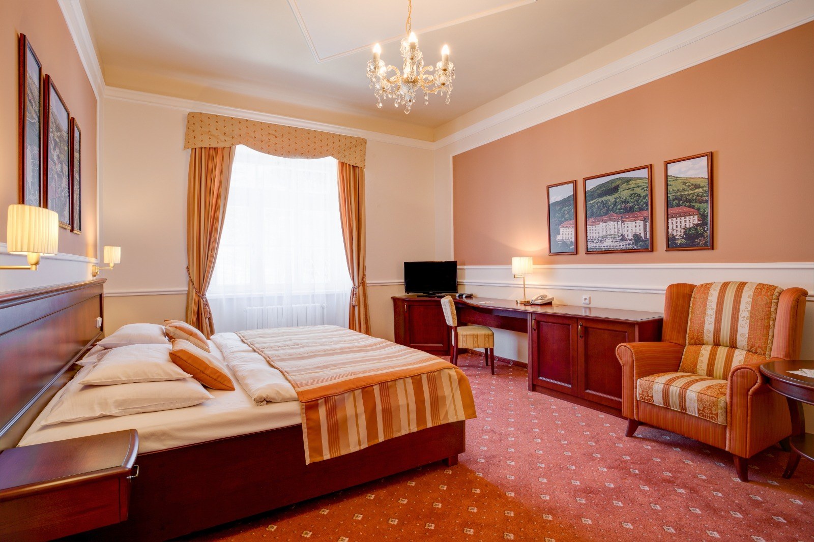 Bedroom interior with striped orange and beige bedding, wooden furniture, an armchair, and wall art above the bed.