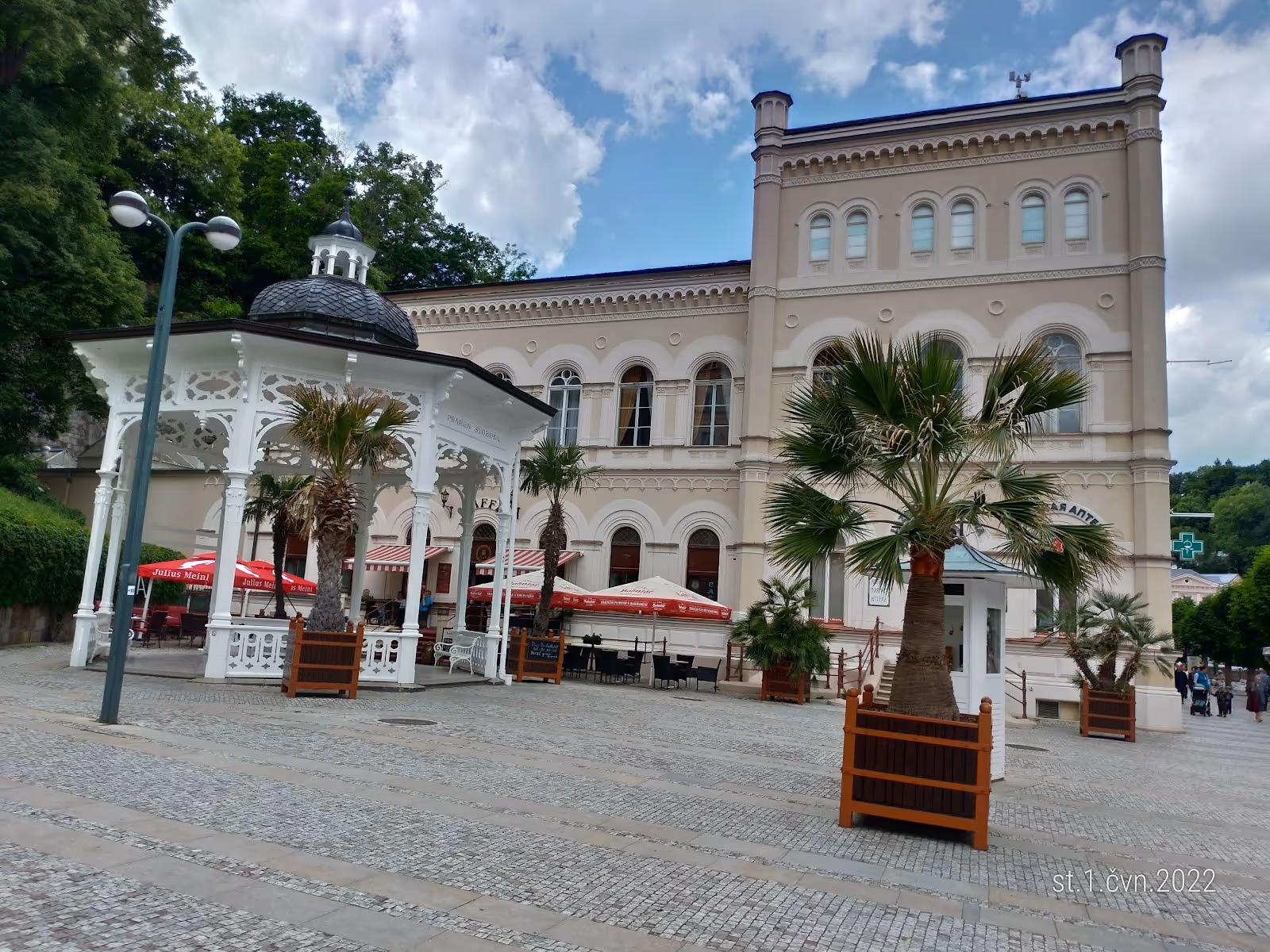 White ornate pavilion with palm trees in large stone-paved square outside Windsor SPA Hotel in Karlovy Vary Czechia.