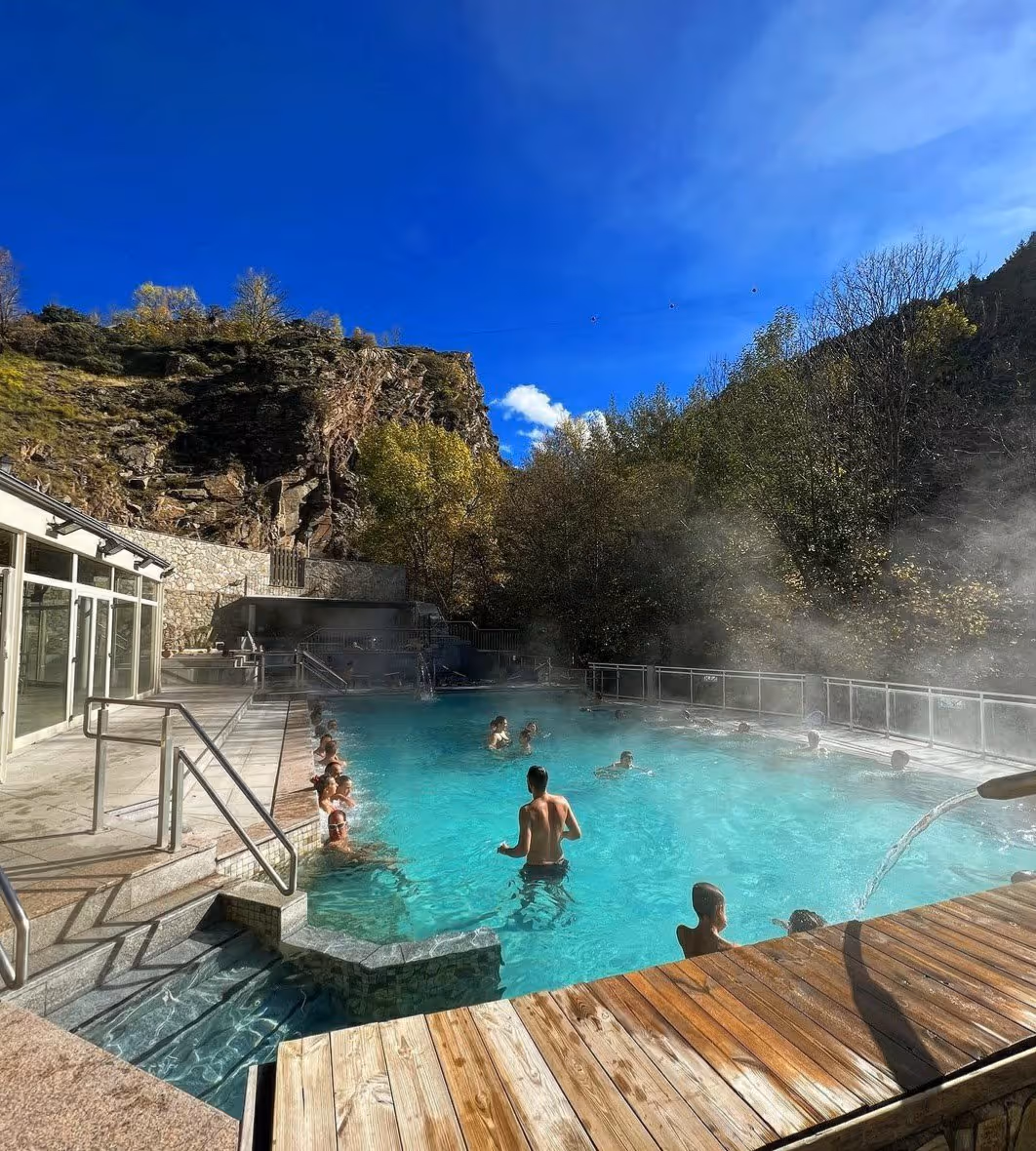 Outdoor hot spring pool at Les Bains de Llo with people soaking under steam and surrounded by rocky hills near Font-Romeu-Odeillo-Via Franc.