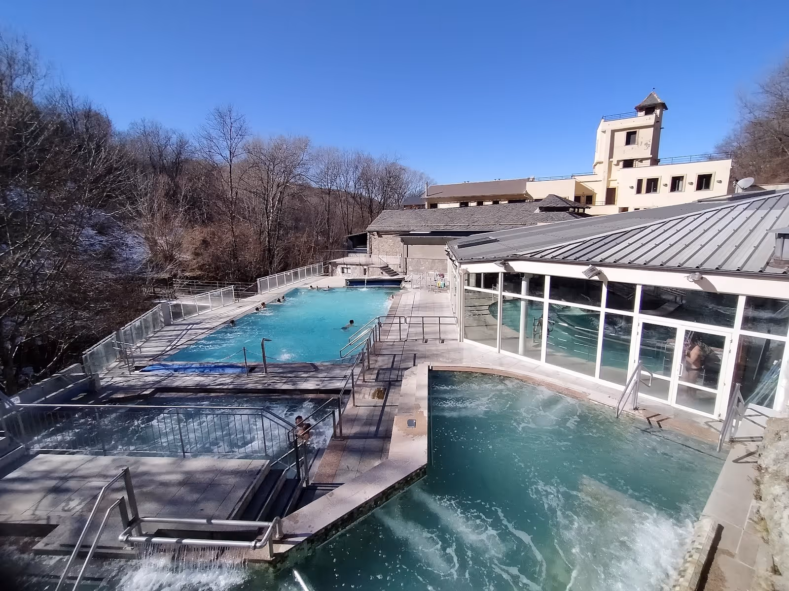 Rectangular outdoor mineral pools at Les Bains de Llo in Font-Romeu-Odeillo-Via with railings and clear blue water on a sunny winter day.