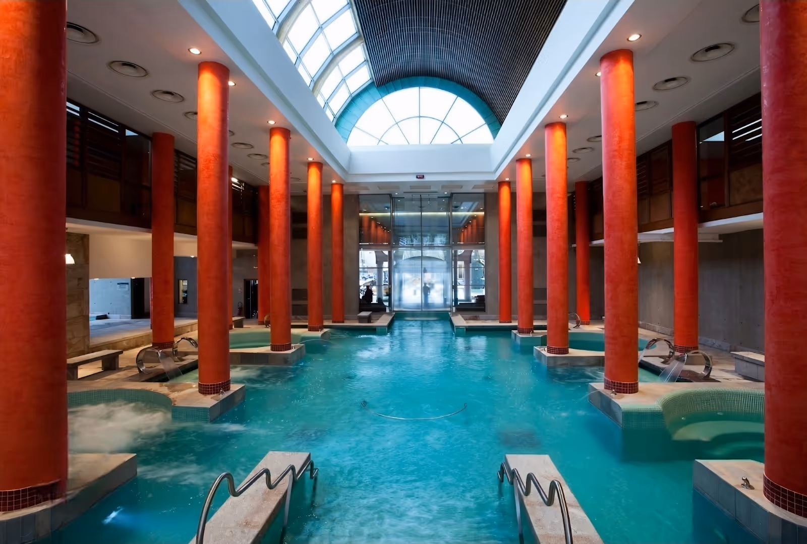 Indoor hot spring pool at Les Bains du Couloubret features tall orange columns and natural light from the arched ceiling in Ax-les-Thermes.