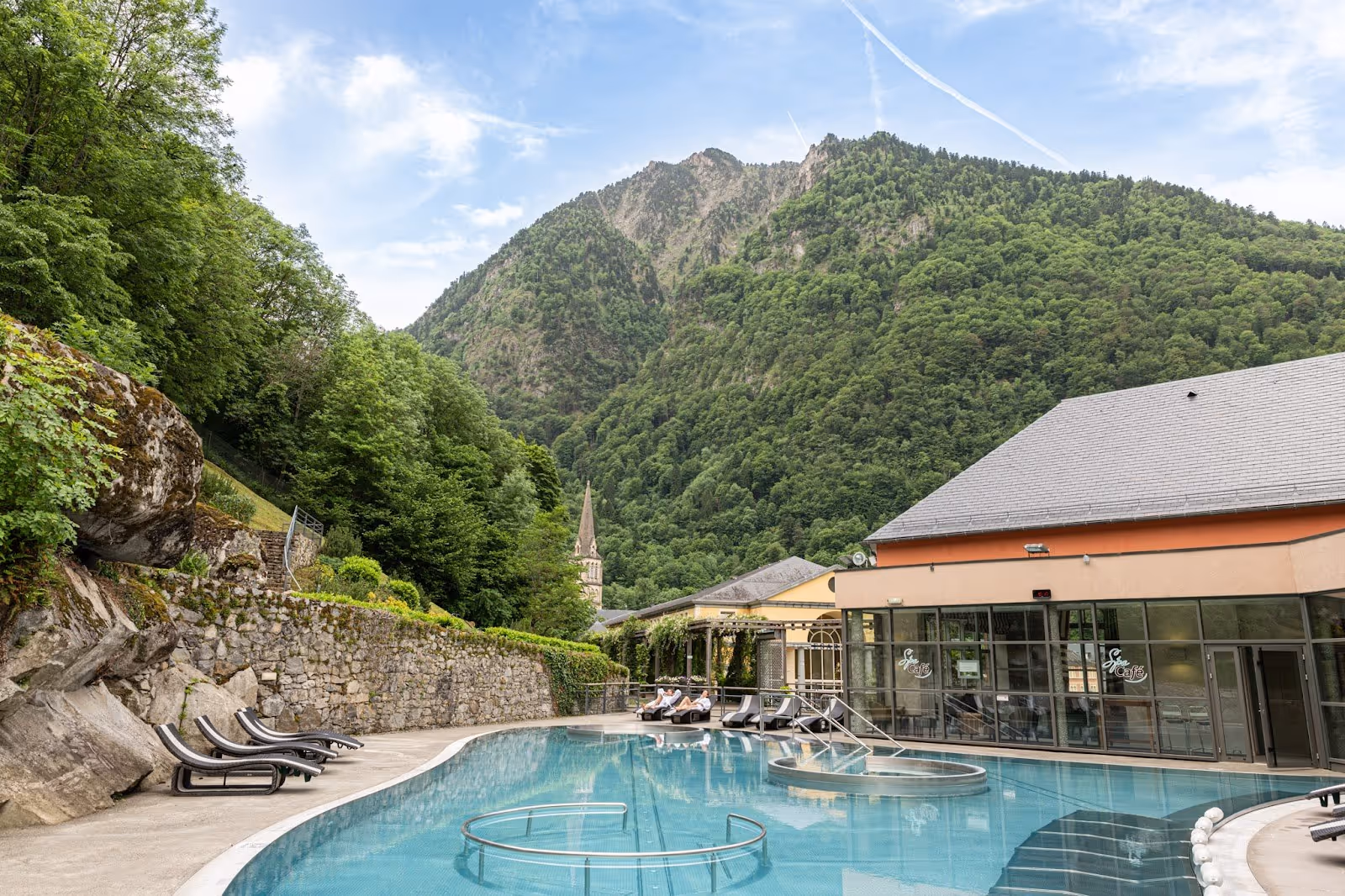 Outdoor mineral pool at Les Bains du Rocher with chairs along poolside and mountain peaks in the background near Cauterets, France.
