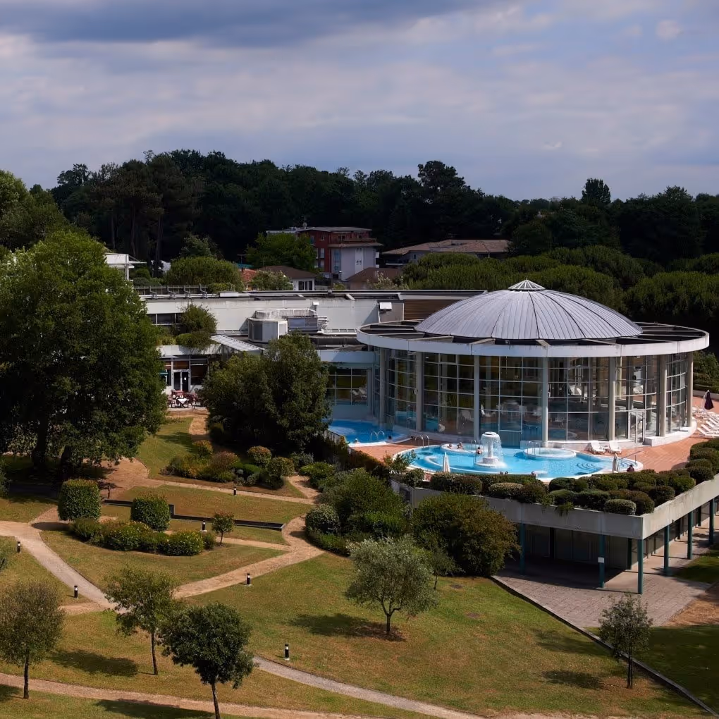 Aerial view of Sourceo hot spring complex in Dax France showing circular glass building with outdoor pools and garden paths.
